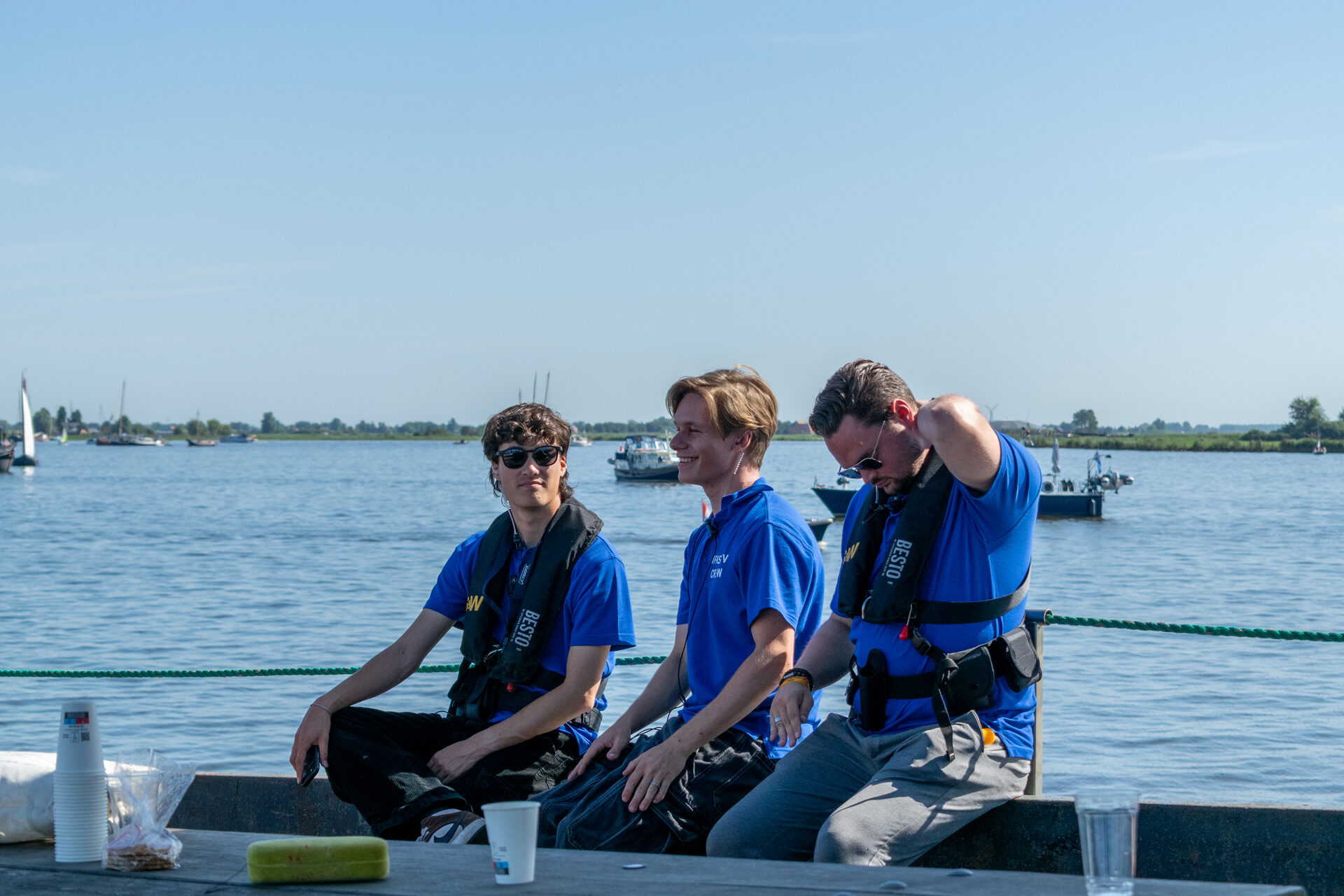 Crew aan de reling van het uitzendschip met de skûtsjes op de achtergrond